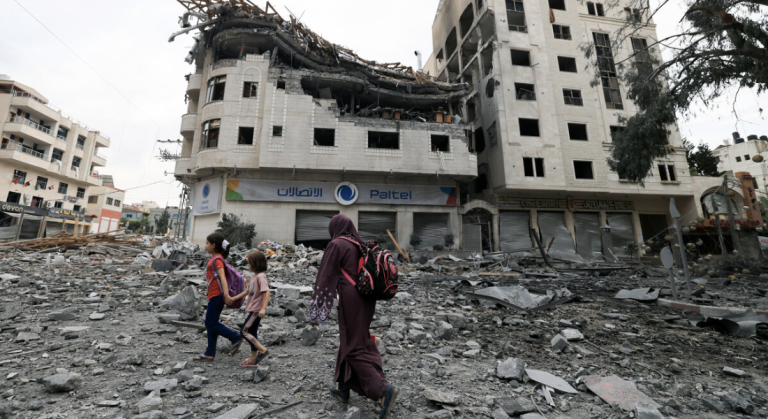 Família palestina caminha diante de ruínas de prédios bombardeados na Faixa de Gaza - Foto: Mahmud Hams/AF