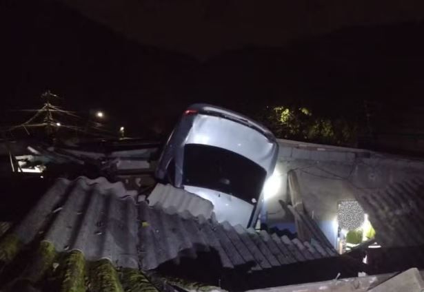 Carro cai em uma casa e fica pendurado em telhado após acidente