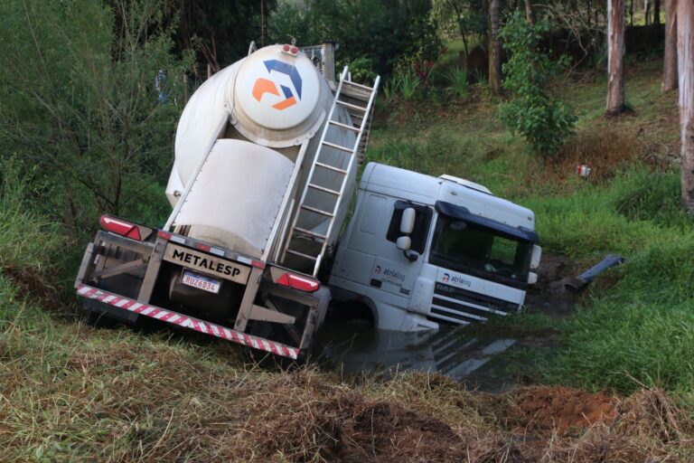Caminhão escorrega em pista molhada, perde controle e fica preso na lama