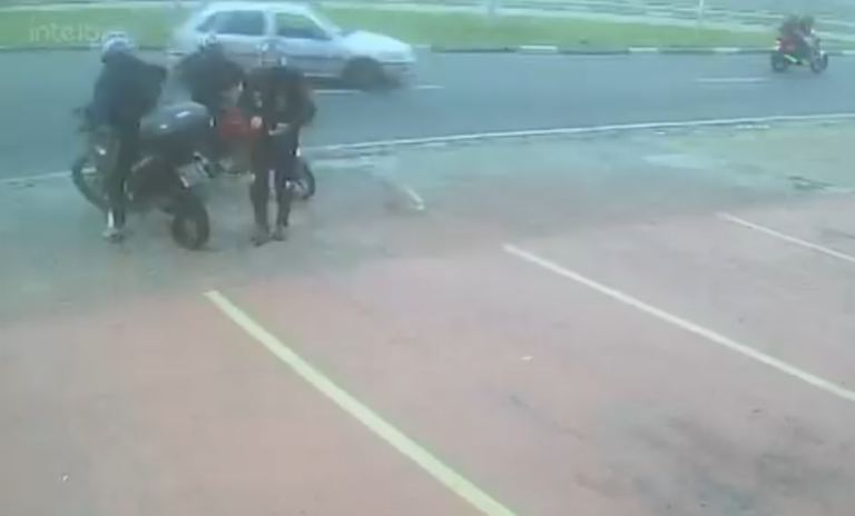 Nas imagens, a vítima aparece em cima da moto, pronta para sair, quando os suspeitos se aproximam em outra motocicleta.