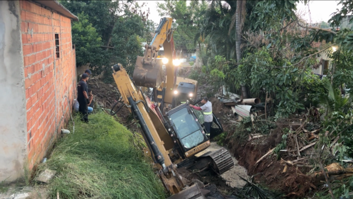 Escavadeira tomba durante limpeza de córrego e atinge muro de casa Escavadeira tomba durante limpeza de córrego e atinge muro de casa